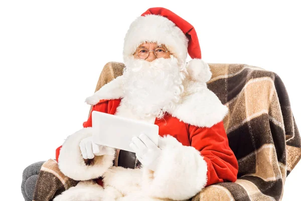 Santa claus sitting in armchair with tablet and looking at camera isolated on white — Stock Photo