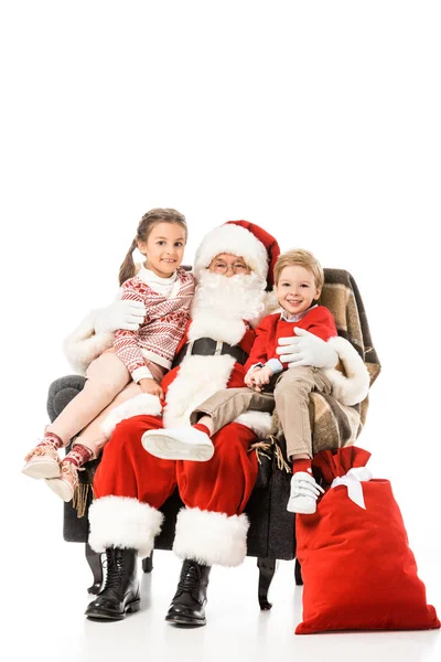 Glückliche Kinder und Santaumarmung und Blick in die Kamera, während sie im Sessel zusammen isoliert auf weiß sitzen — Stockfoto