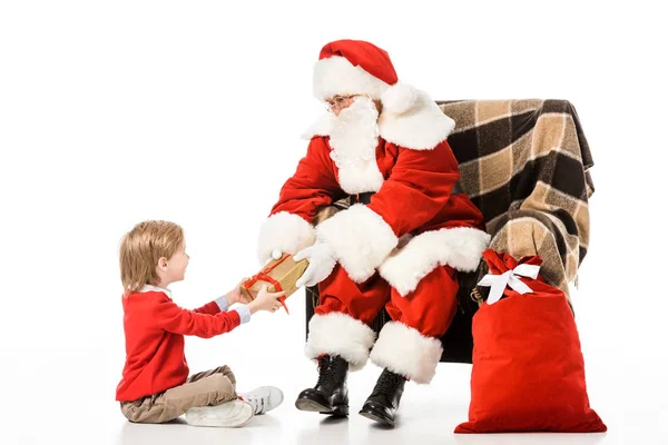 Santa presenting christmas gift to kid while sitting in armchair isolated on white — Stock Photo