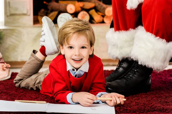 Happy little kid drawing on carpet near santa — Stock Photo