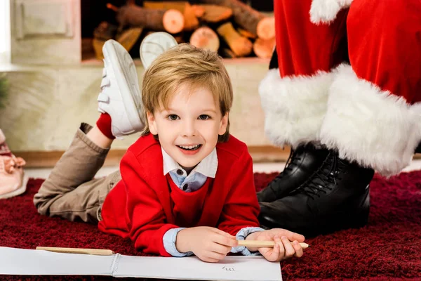 Criança feliz desenho no tapete perto de santa — Fotografia de Stock