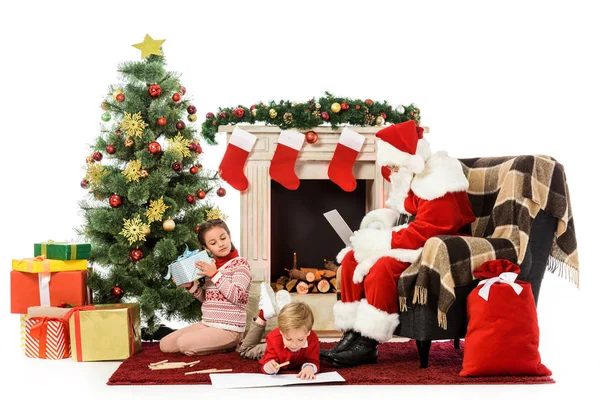 Kinder beim Auspacken von Geschenken und Zeichnen am Boden in der Nähe des Weihnachtsmannes im Sessel — Stockfoto