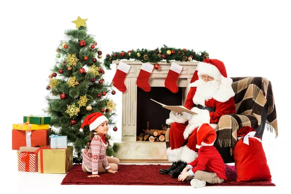 Santa reading book for kids while sitting in armchair isolated on white — Stock Photo