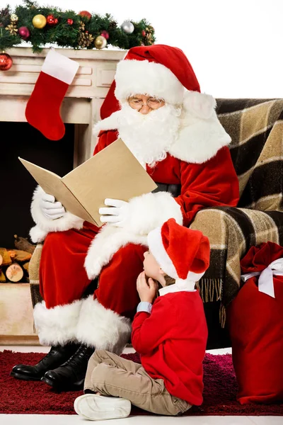 Santa reading book to little kid while he sitting on carpet — Stock Photo