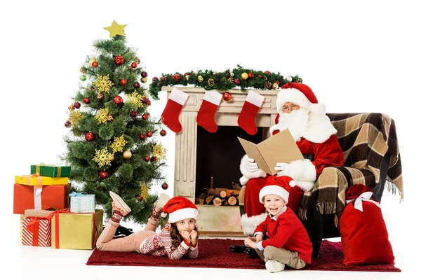 Kids and santa looking at camera while relaxing in front of fireplace isolated on white — Stock Photo