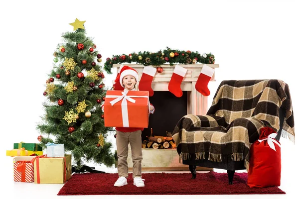 Усміхнений маленький хлопчик тримає великий червоний різдвяний подарунок і дивиться на камеру ізольовано на білому — стокове фото