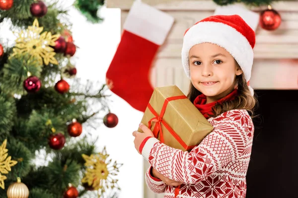 Schönes kleines Kind mit Weihnachtsgeschenk und Blick in die Kamera — Stockfoto