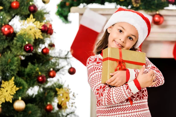 Linda criança segurando presente de Natal e olhando para a câmera — Fotografia de Stock