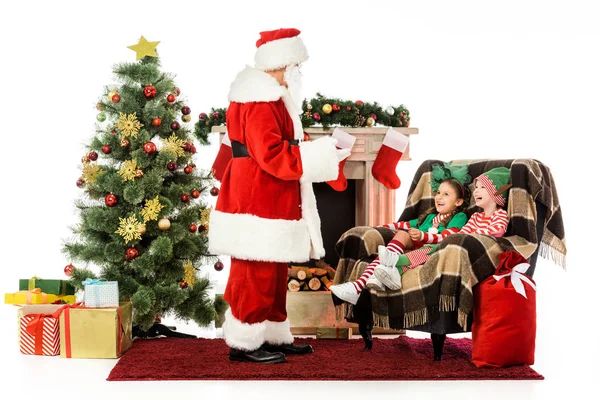 Санта разговаривает с детьми, пока они сидят в его кресле изолированы на белом — стоковое фото