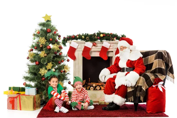 Excited kids and santa sitting in front of fireplace together isolated on white — Stock Photo