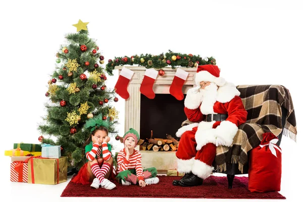 Gelangweilte Kinder und Weihnachtsmann sitzen gemeinsam vor dem Kamin, isoliert auf weißem Grund — Stockfoto