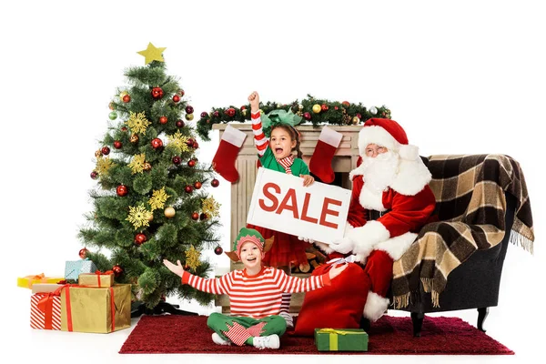 Happy kids in elf costumes and santa holding sale banner, christmas shopping — Stock Photo