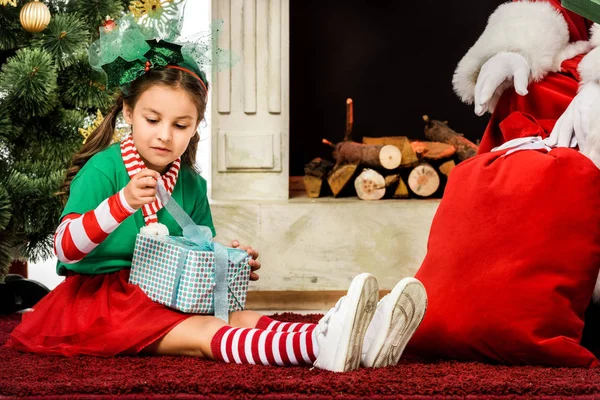 Adorable niño pequeño sentado en la alfombra con regalo de Navidad cerca de santa - foto de stock