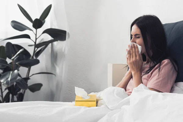 Malade jeune femme avec boîte de serviettes en papier assis dans le lit — Photo de stock