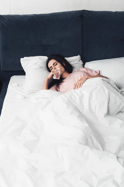 Sick young woman with runny nose lying in bed with napkins — Stock Photo