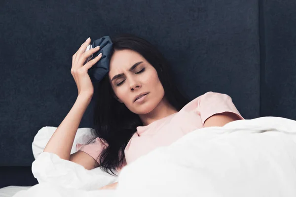Kranke junge Frau mit Eisbeutel auf Kopf im Bett liegend — Stockfoto