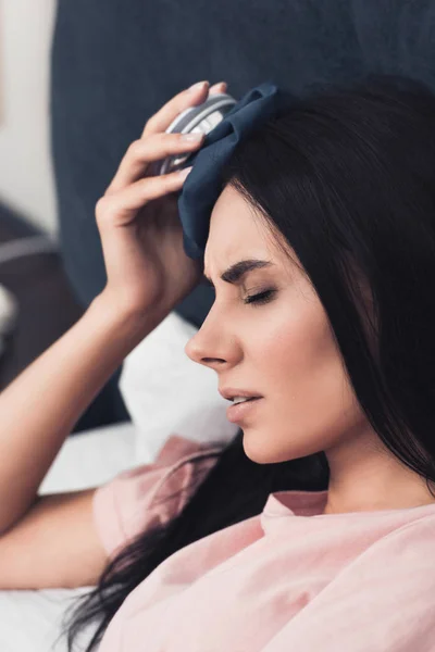 Close-up shot of sick young woman holding ice pack on head while lying in bed — Stock Photo