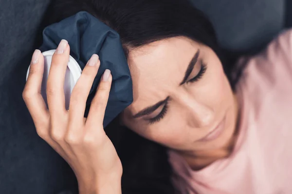 Крупный план больной молодой женщины, держащей пакет со льдом на голове, лежащей в постели — стоковое фото
