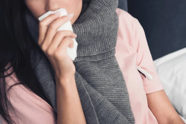 Cropped shot of sick young woman covering mouth with napkin during cough in bed — Stock Photo
