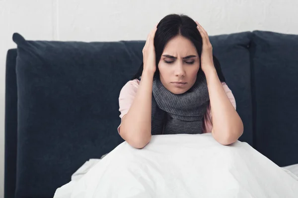 Mujer joven enferma sentada en la cama y sosteniendo la cabeza durante el dolor de cabeza - foto de stock