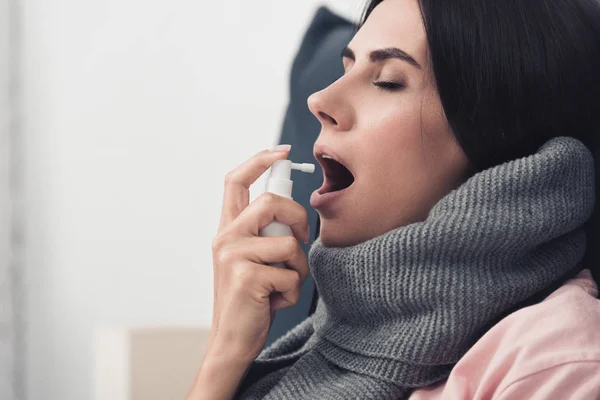 Malade jeune femme en écharpe à l'aide de spray contre la toux — Photo de stock