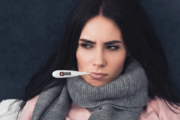 Хвора молода жінка вимірює температуру з термометром електронного рота і дивиться вниз — стокове фото