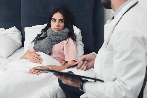 Schnittwunden an junger Frau, die im Bett liegt, während Arzt Klemmbrett hält — Stockfoto