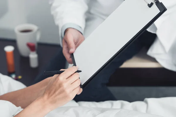 Plan recadré du médecin donnant presse-papiers avec des documents au patient à signer — Photo de stock