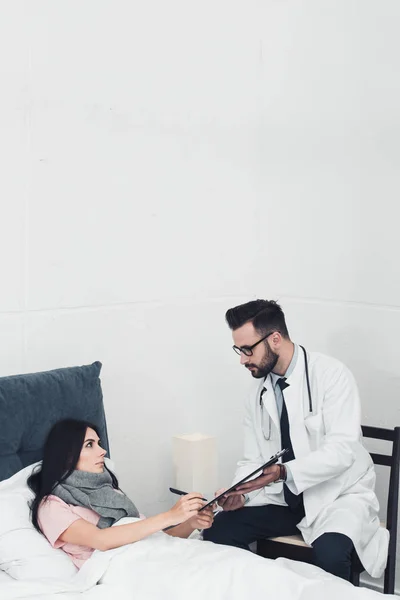 Schöner Arzt gibt Klemmbrett mit Dokumenten an Patienten zum Unterschreiben — Stockfoto