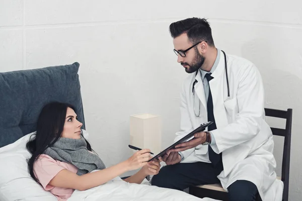 Young doctor giving clipboard with documents to patient to sign — Stock Photo