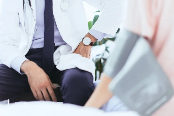 Cropped shot of doctor sitting in front of patient with blood pressure gauge on hand — Stock Photo