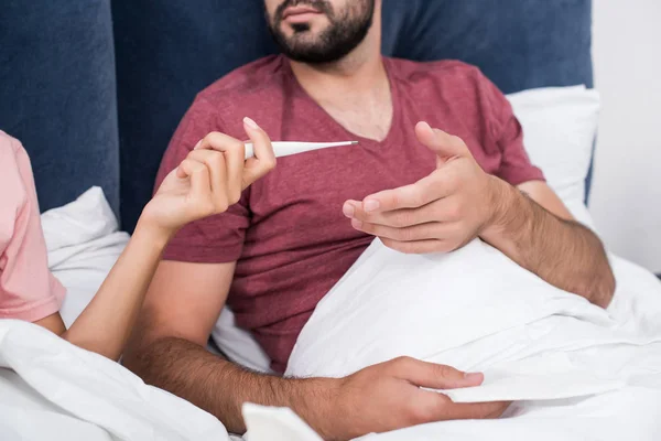 Plan recadré de femme passant thermomètre électrique à son copain malade au lit — Photo de stock