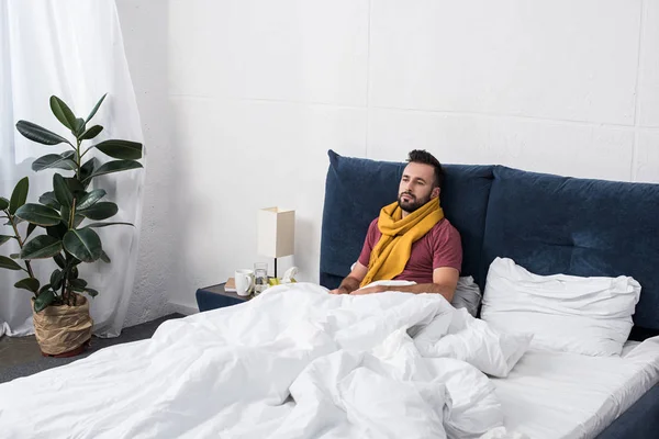 Deprimido doente jovem deitado na cama em cachecol e olhando para longe — Fotografia de Stock