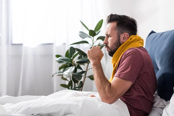 Side view of sick young man having cough while sitting in bed — Stock Photo