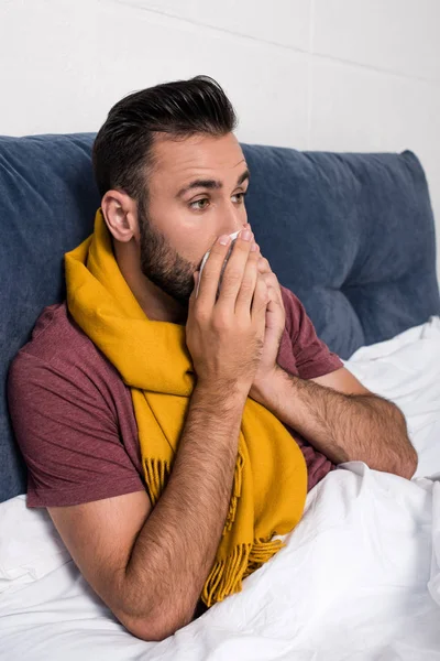 Malade jeune homme éternuer tout allongé dans le lit — Photo de stock