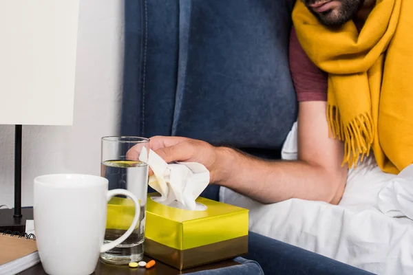 Cropped shot of sick young man taking paper napkins from box while lying in bed — Stock Photo