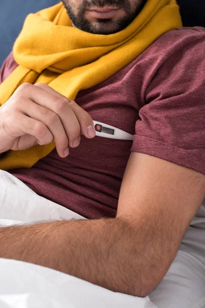 Cropped shot of sick man measuring temperature with electronic thermometer in bed — Stock Photo