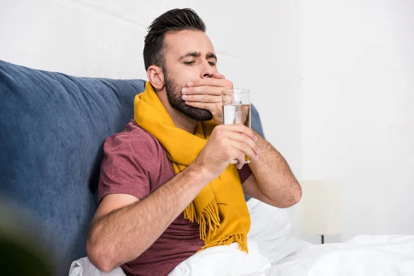 Joven enfermo tomando pastillas mientras está sentado en la cama - foto de stock