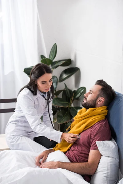 Ärztin mit Stethoskop, um Patienten beim Atmen zuzuhören, während er im Bett liegt — Stockfoto