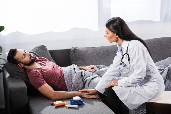 Médico feminino segurando a mão do paciente enquanto ele deitado no sofá — Fotografia de Stock