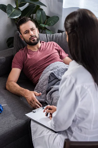 Vista posteriore del medico donna con appunti seduto vicino paziente sofferente — Foto stock