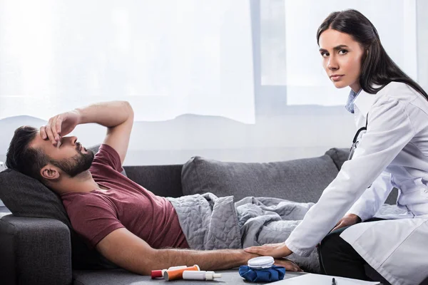 Женщина-врач держит пациента за руку и смотрит в камеру, пока он лежит на диване — стоковое фото