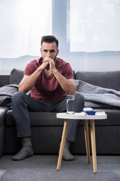 Депресивний молодий чоловік сидить на дивані і думає з ліками на столі — стокове фото