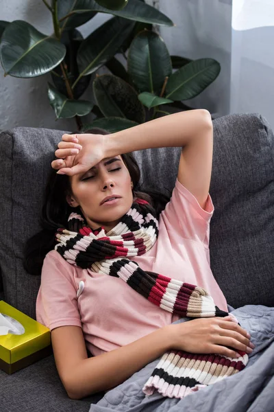 Malato giovane donna con sciarpa sdraiato sul divano a casa — Foto stock