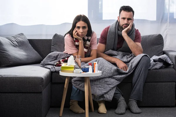 Diseased young couple with meds on table sitting together on couch — Stock Photo