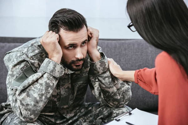 Soldado deprimido con síndrome postraumático mirando al psiquiatra durante la sesión - foto de stock