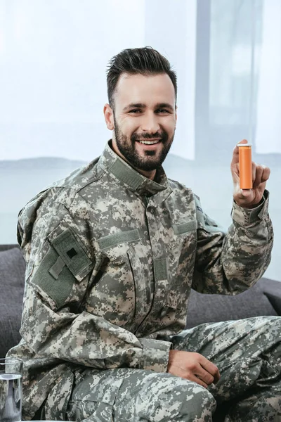 Feliz joven soldado sosteniendo frasco de plástico de píldoras y mirando a la cámara - foto de stock