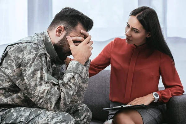 Soldado y psiquiatra sentado en el sofá durante la sesión de terapia - foto de stock