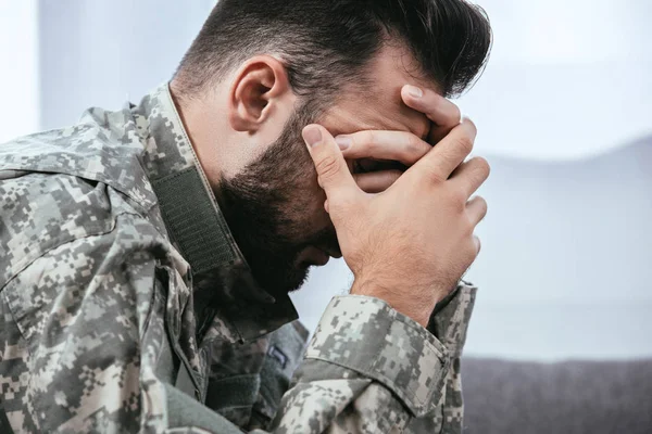 Seitenansicht eines depressiven Armeeangehörigen in Militäruniform mit posttraumatischer Belastungsstörung, der seinen Kopf hält — Stockfoto