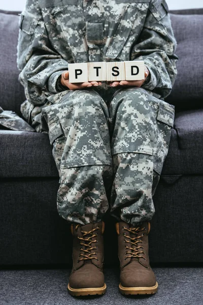 Recortado disparo de soldado femenino en uniforme militar sentado en el sofá y la celebración de cubos de madera con signo de PTSD - foto de stock